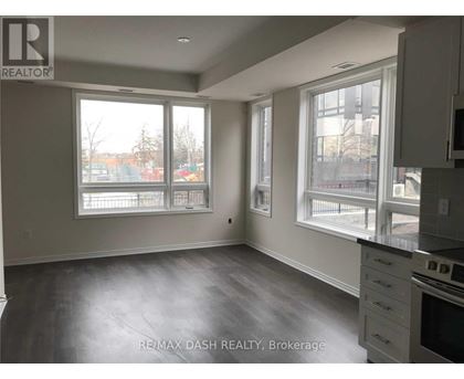 A spacious room with a grey floor and white walls, featuring a kitchen area with a stove and cabinets.