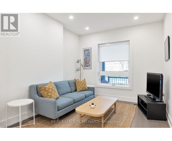A living room with a grey couch, a white side table, a wooden coffee table, and a flat screen TV.