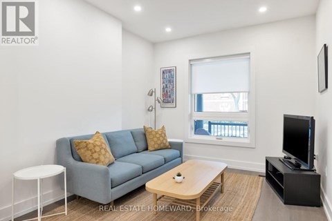 A living room with a grey couch, a white side table, a wooden coffee table, and a flat screen TV.