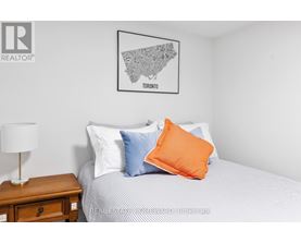 A bedroom with a bed, a nightstand with a lamp, and a framed map of Toronto on the wall.