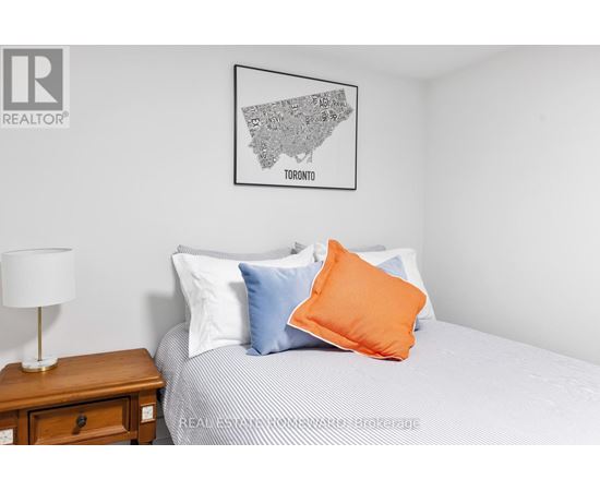 A bedroom with a bed, a nightstand with a lamp, and a framed map of Toronto on the wall.