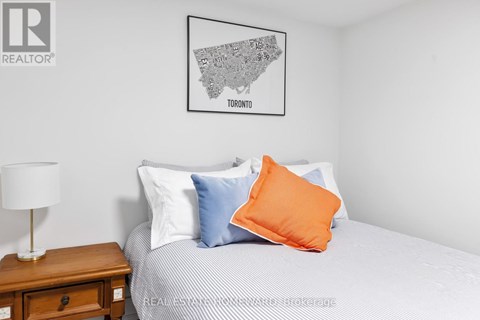A bedroom with a bed, a nightstand with a lamp, and a framed map of Toronto on the wall.