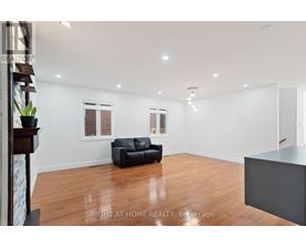 A spacious living room with a black leather sofa and wooden flooring.
