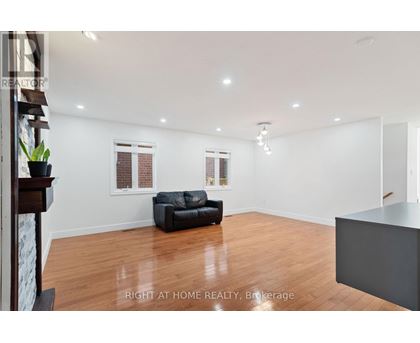 A spacious living room with a black leather sofa and wooden flooring.