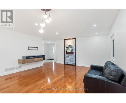 A spacious living room with a black leather couch and wooden flooring.