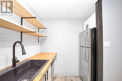 A kitchen with a sink, refrigerator, and wooden shelves.