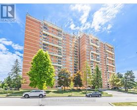 A large red brick apartment building with a tree in front and cars parked in front.