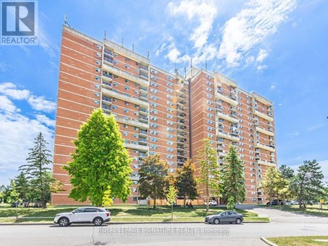 A large red brick apartment building with a tree in front and cars parked in front.
