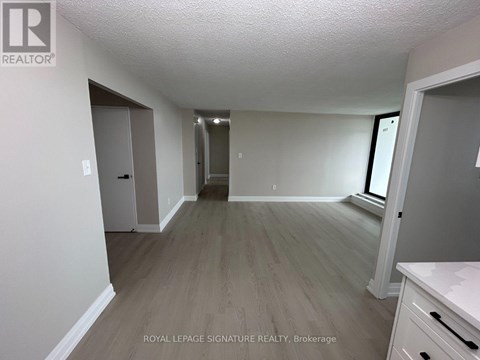 A room with a white ceiling and wooden flooring with a door on the left and a window on the right.
