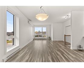 A spacious room with wooden floors and a large window overlooking a residential area.