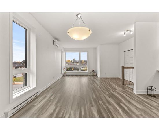 A spacious room with wooden floors and a large window overlooking a residential area.
