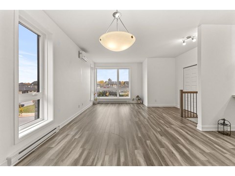 A spacious room with wooden floors and a large window overlooking a residential area.