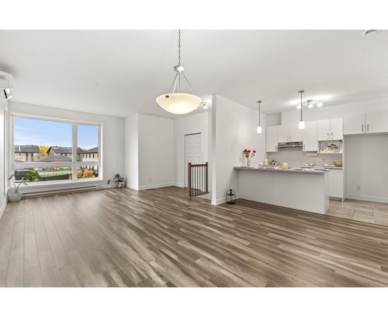 A spacious kitchen and living room with wooden flooring and white walls.