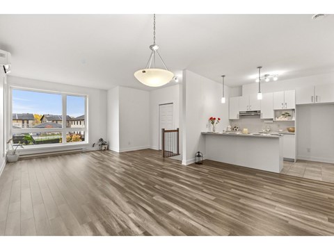 A spacious kitchen and living room with wooden flooring and white walls.