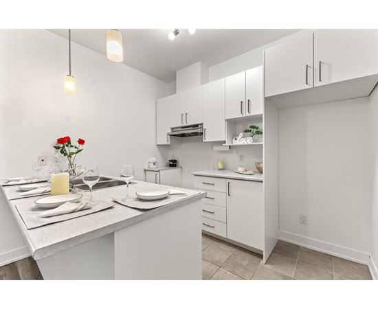 A kitchen with a table set for two with a vase of red roses.