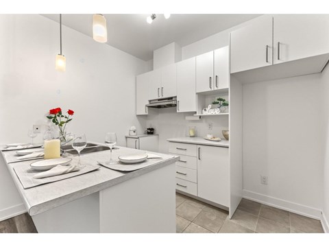 A kitchen with a table set for two with a vase of red roses.