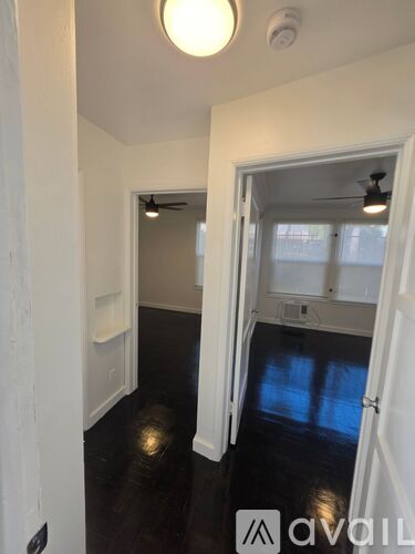 A hallway with a light on and a door open to a room with a ceiling fan.