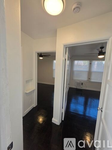 A hallway with a light on and a door open to a room with a ceiling fan.
