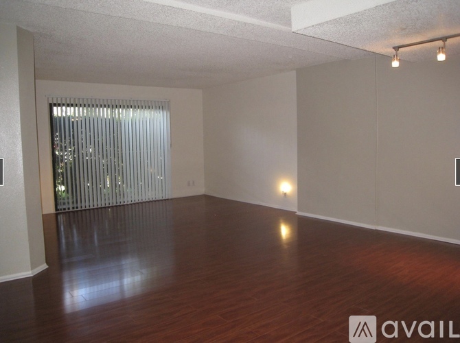 A spacious room with wooden floors and a window with blinds.