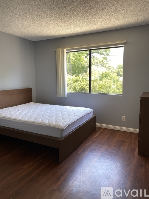 A bedroom with a bed, wooden floors, and a window with a view of trees outside.