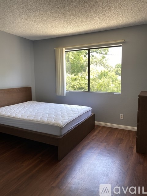 A bedroom with a bed, wooden floors, and a window with a view of trees outside.