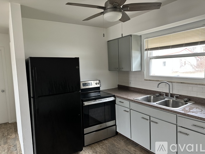 A black refrigerator stands in a kitchen with a stove and oven.
