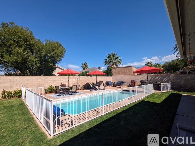 A pool surrounded by a white fence with red umbrellas in the background.
