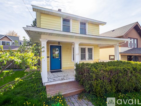A yellow house with a blue door and a green bush in front.