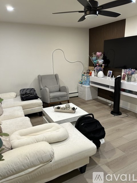 A living room with a white couch, a grey armchair, a television, and a fan.
