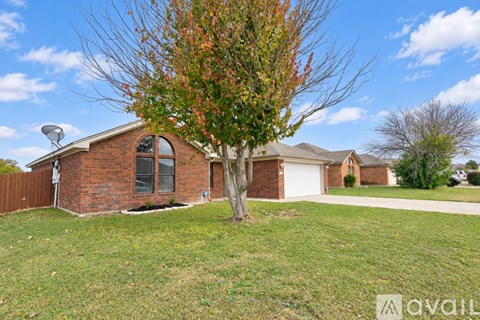 A tree with red leaves stands in front of a brick house.
