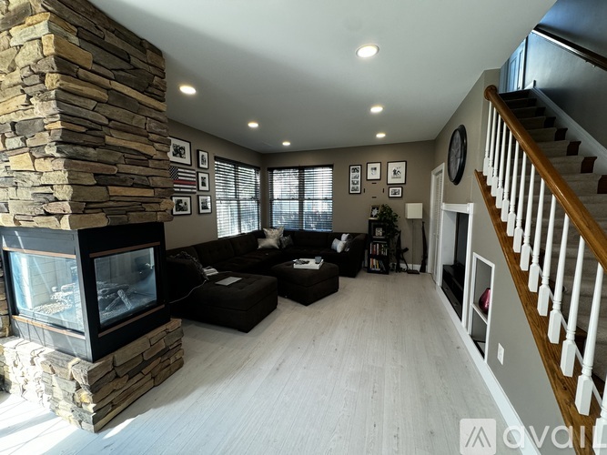 A living room with a stone fireplace and a staircase.