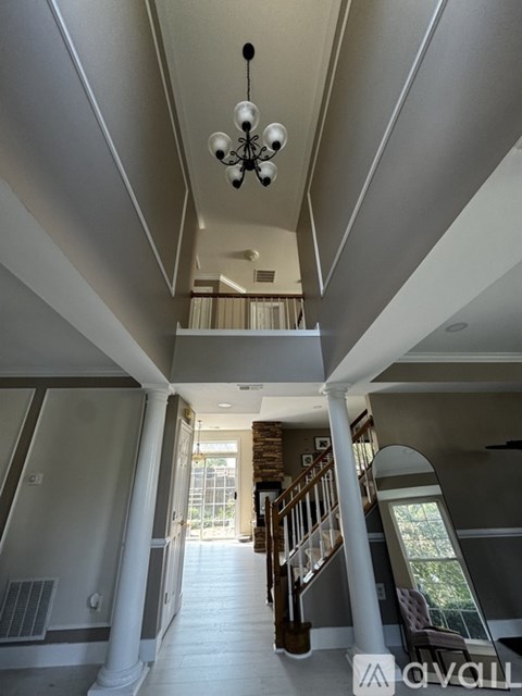 A chandelier hangs from the ceiling in a spacious room with white columns and a staircase.