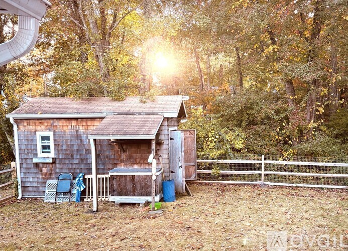 A small wooden shed with a porch and a white fence in the background.