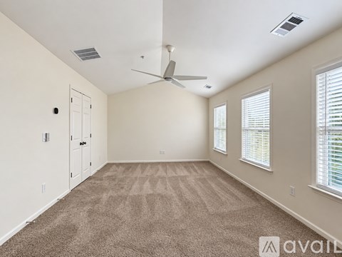 A spacious room with a carpeted floor, a ceiling fan, and a window with blinds.
