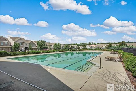 A large outdoor swimming pool surrounded by a concrete deck and lounge chairs.