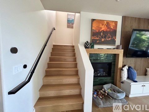 A staircase with a black handrail and wooden steps leads to a living room with a fireplace and a painting on the wall.