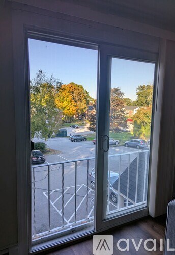 A view from inside a room looking out through a window to a parking lot and trees.