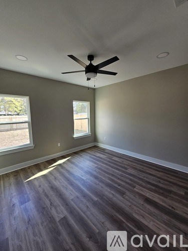 A room with a ceiling fan and two windows.