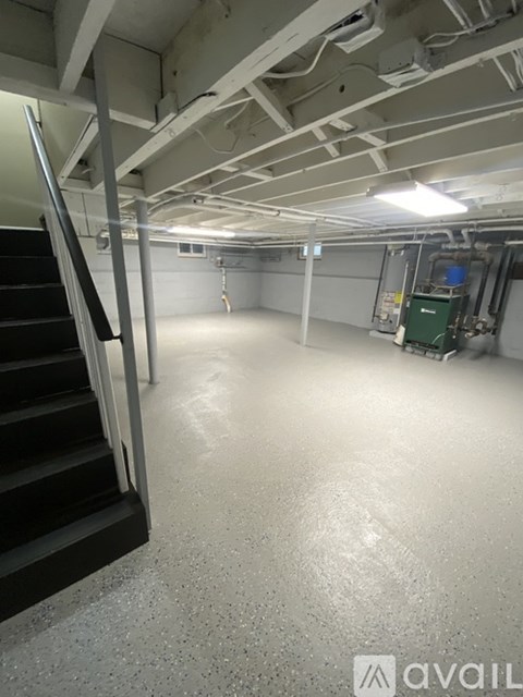 A spacious, empty industrial-style room with a staircase on the left and a green machine on the right.
