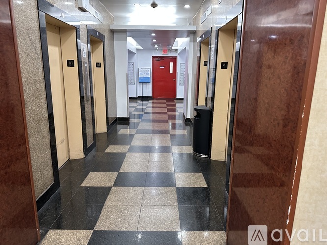 A hallway with a black and white checkered floor and a red door at the end.