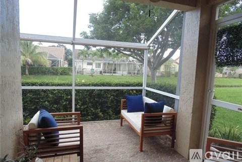 A patio with a couch and a chair with a view of a backyard.
