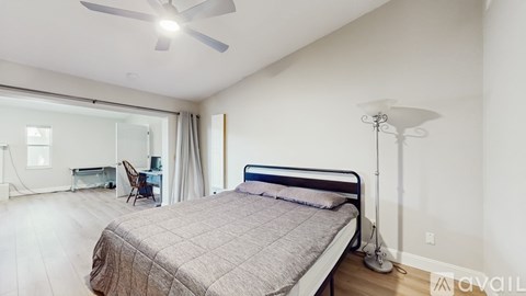 A bedroom with a bed, desk, chair, and ceiling fan.