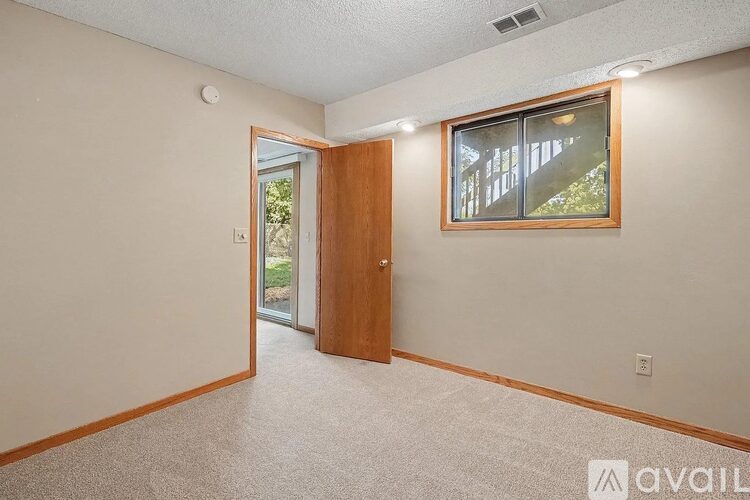 A room with a carpeted floor, a wooden door, and a window with a view of trees.