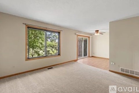 A spacious room with a window, carpet, and a ceiling fan.