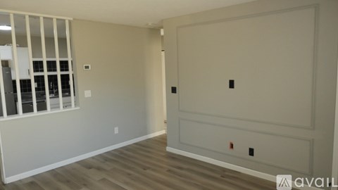 A room with a white door, a window with bars, and a wooden floor.
