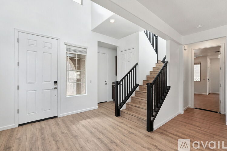 A spacious room with wooden floors and a staircase with black railings.