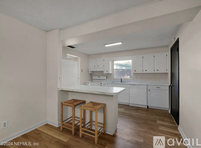 A kitchen with white cabinets and a bar area with stools.