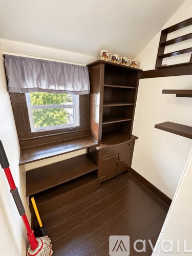 A room with a window, a broom, and a shelf.