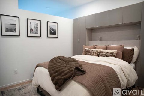 A bedroom with a bed covered in a white and brown comforter and pillows, a brown blanket, and three framed pictures on the wall.