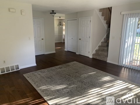 A living room with a rug on the floor and a staircase in the background.